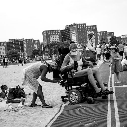 Nolan Ryan Trowe, VII Mentor Program, July 4, 2018; Coney Island, Brooklyn: A woman struggles to help her mother back onto the accessible path after her wheels sunk into the sand, by lifting her power wheelchair.