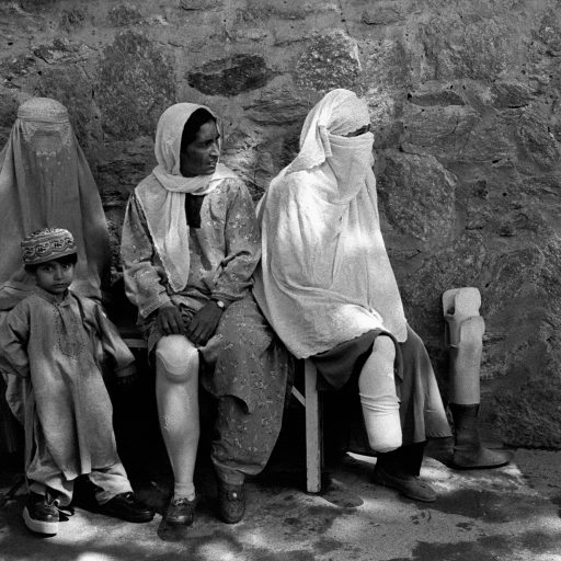 Orthopedic center, Afghanistan, March 2003.Three woman with prosthetic devices are sitting on a bench outside the center with a child.The majority of patient amputees is victim of mines.The center is in operation in Kabul since 1988.