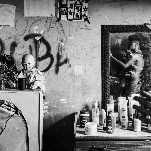 In February, 2015, a woman shows her home inside of the IBGE buildings, a part of the Favela da Mangueira. On the little desk, a variety of beauty products that she collected in other people’s garbage as she walks all around Rio de Janeiro. Even though the occupants are forgotten by the local government and suffer all kinds of prejudice, some of them can still maintain their vanity. The drawings on the wall show a large family and that she needs to do anything to provide for them. Mangueira is one of the most famous favelas in Rio de Janeiro for its tradition in samba. It is located in Rio's north zone, a few steps away from Maracana, the biggest football stadium in the city, which received near two billion Reais on public investments for the 2014 World Cup. The misdirection on the government attention, makes the abandoned building, a social disaster as they don't have piped water, collection of garbage or any other public service.