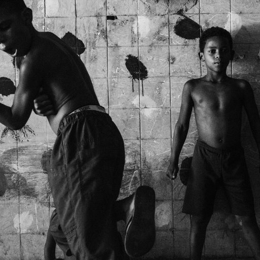 In July, 2014, two young boys dance and play in one of the abandoned rooms inside the IBGE building, a part of the Favela da Mangueira. The painted dots on the wall were made by the occupants in a try to decorate some of the broken walls in their own way. Despite the harsh conditions and the wrecks surrounding them, the children who live in IBGE still have inside themselves a magical touch as they are able to play and sometimes still have a good time. Mangueira is one of the most famous favelas in Rio de Janeiro for its tradition in samba. It is located in Rio's north zone, a few steps away from Maracana, the biggest football stadium in the city, which received near two billion Reais on public investments for the 2014 World Cup. The misdirection on the government attention, makes the abandoned building, a social disaster as they don't have piped water, collection of garbage or any other public service.