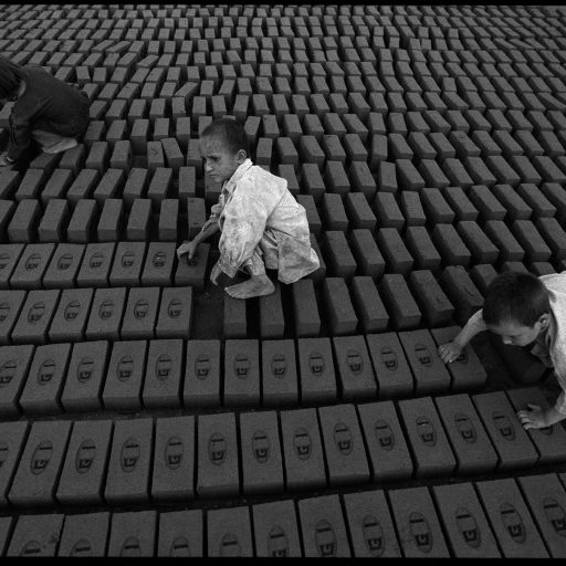 Children tilt bricks up on their side after two days of drying at the GT Brick factory in Karkhla, Pakistan, October 2001. The children, aged 4-6, perform this labor for their father because they are lightweight and do not deform the bricks which are still somewhat soft.