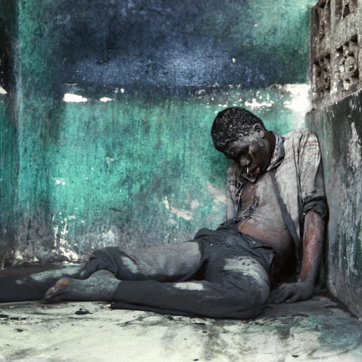 The body of a man lays in a small alcove along a well-traveled pathway in Cite Soleil slum in Pt-au-Prince,Haiti. 1987. During weeks leading up to the first democratic elections in 30 years, after the fall of the Duvalier Family dictatorship in Febuary 1986, shooting could be heard throughout the capital and in other cities all night long. In the mornings Haitians would venture out and find bodies of people shot at night by gangs of menopposed to the elections and changes. The murders were meant to scare people from casting their voteson election day in November 1987.