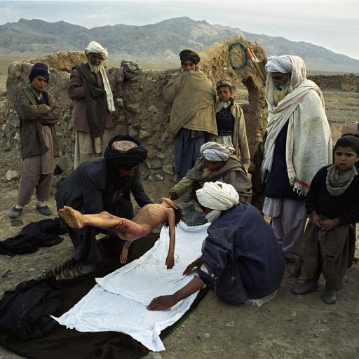 An Afghan family seen preparing the body of an eight-year-old boy who died from the cold at the Maslakh refugee camp near Herat, Afghanistan, Feb. 15, 2001. The boy's uncles place the body on a white sheet as family members look on.Photo by: Alexandra Boulat / VII