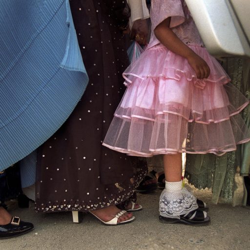 Heading to a wedding party in Kabul, women of all ages get in a car, displaying  different fashion styles:  At left, a  burka coverings dark blue  pants follows a fancy dress worn by a 30 year old.  No burka and even more style for the young adults at right,  and a pink lace dress on a  five-year-old girl.