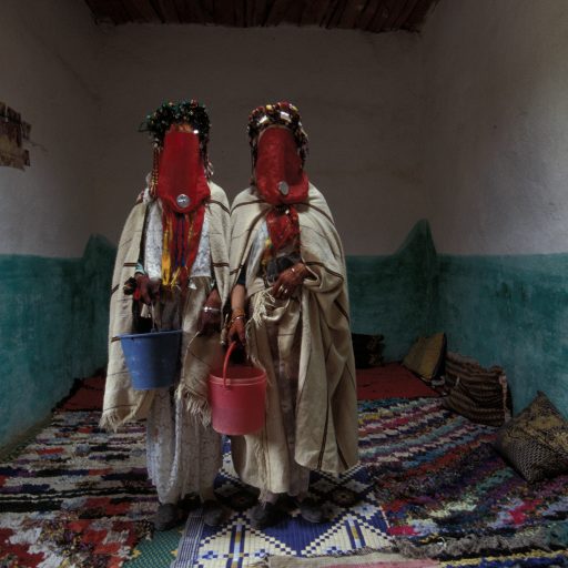 Two young brides gather for a 3 day long mass wedding ceremony in the Berber village of Taaraart, Morocco, in which 18 couples will be married, Sep. 2003. On the third day of the wedding, brides covered with traditional wool blankets and red veils go to the river together to get some water as a purification ritual.  Few men manage to choose women outside their village, however, the families concerned normally agree on pairings that are not in the same family.Photo by: Alexandra Boulat / VIIMarocco: Berbers of the High Atlas, two brides at home during the Mass wedding ceremonies, 3 days long to marry 18 couple, by the Ait Ayach people in Taaraart. September 2003. On the third day of the wedding, brides covered with traditional wool blankets an a red viel go to the river together to get some water, as a purification ritual. Taarart village, 2000 inhabitants, in the Djebel Ayachi range, East of the High Atlas. After the harvest, not every year, but when ever it has enough couple to marry, Taarart gets organized for 3 days party to marry its couple.  One could see it as inbreeding weddings, but at some point, few men manage  to choose women outside their village (they marry them in Taarart), and for the one who choose their life partners inside the village, the families concerned managed to agree for weedings which are not relatives inside the same family. Those wedding customs are tribal and ancient Berber tribal custom, with a muslim/Arabic culture influence.  Photo © Alexandra Boulat