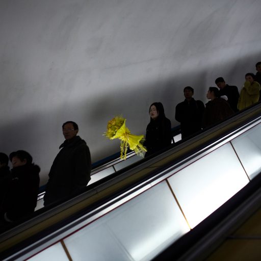 Behind the Curtains series — A Korean woman carries a bouquet of yellow flowers down the escalator into the Pyongyang metro subway, North Korea.