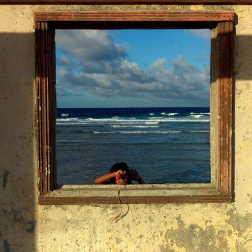 A child looks through the window frame of a partially destroyed abandoned home on the Pacific shore of Ebeye, Marshall Islands. Over 12,000 people live on the tiny overcrowded island of 36 hectares. The islanders relocated to Ebeye from their original homes because the U.S. military leases those areas for ballistic missile testing. Other current residents of Ebeye moved from islands which were contaminated by U.S. nuclear bomb tests. Infrastructure, housing and sanitation on Ebeye are deplorable.