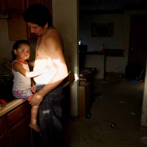 Caption:  Father and daughter, Allen, Pine Ridge Reservation.  Allen has been called the poorest town in America and is part of the Pine Ridge Reservation.  Over 90 percent of Pine Ridge residents live below the federal poverty line, and the unemployment rate hovers between 85 and 90 percent.       
     

     Story Summary:  The Badlands of South Dakota are surrounded by one of the most economically depressed regions in the United States.  While economic and social strife are commonplace in the Badlands, this is also a section of the country rich with culture and traditional life.  Much of the Badlands are part of the Pine Ridge Reservation, home of the Oglala Lakota, a tribe once led by the legendary war chief Crazy Horse.  Pine Ridge is also where some 300 men, women, and children were slaughtered by the U.S. 7th Calvary at the Massacre of Wounded Knee in 1890, the tragic end to the Indian Wars. 

     Conditions on the Pine Ridge Reservation are equal to the most impoverished nations in the world.  Over 90 percent of Pine Ridge residents live below the federal poverty line, and the unemployment rate hovers between 85 and 90 percent.  Life expectancy is 48 years for men and 52 for woman.  Though faced with staggering poverty, many Lakotas work to preserve traditional culture and maintain their community.

     Lakotas are not the only people who struggle economically in the region today.  Small towns across the Badlands have suffered greatly as an economic shift in America has bankrupted and depopulated many rural communities.  Broken-down ranches litter the landscape, while leather-faced cowboys seemingly as old as the soil itself pass in sun-faded pickups.  Many ranchers in South Dakota are descendants of the land-hungry settlers who pressured the U.S. government to take Lakota territory and confine the Sioux to reservations.  Now both Indians and whites are living in isolation in the Badlands, forgotten communities left to survive if they can.