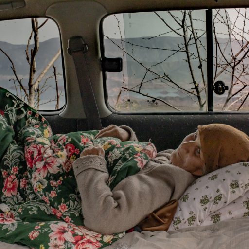 Tajikistan: With Norak reservoir seen in the background, Ranobi Islomova, 63, who is ill, waits in a car to continue her trip to a neighboring town. The reservoir was formed by the Norak Dam, the tallest in Tajikistan.