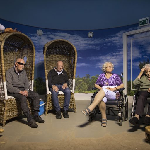 HAARLEM, THE NETHERLANDS - 1 MAY, 2018: The beach room in care facility De Houttuinen in Haarlem, The Netherlands. The beach room has real sand on the floor, the sound of waves, heat regulating lamps, wind, beach seats and sun screen. 
People with dementia living at De Houttuinen go to the beach room for a calming and relaxing experience. Elderly people from left to right: Arnold Piek (79), Ronne Zwart (74), Jo Franke (82) and Riet van Driel (93).