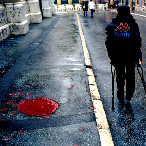 Street scene, Sarajevo. At left is a "rose" of Sarajevo, which marks one of the mortar blasts fired at the city by Serb forces. Mortar blasts leave a pattern that looks like a flower; after the war, blasts that killed large numbers of people were filled in with red as a commemoration to those who died. September, 2002.