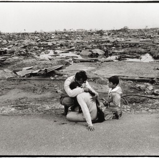 An Acehnese man consoles a woman whom I presume is his wife or sister. immediately behind them is the concrete foundation of the home where they once lived. On the horizon, is the town centre of banda Aceh.