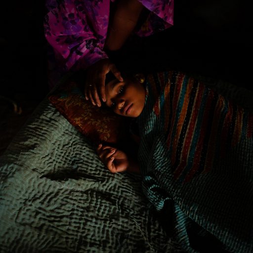 Bharti, 12, rests at home under the care of her mother Ramsabha, to reduce the fever and the severe headaches. Madhya Pradesh, India. 

Ramsabha Bai, 36, was raped by her boss. She was threatened with a knife to the neck and with her daughter Bharti as a witness. “My daughter got awake, silent and afraid in a corner of the room, telling me not to scream or the attacker would kill us both. [...] She went to the side and covered her face with a blanket and quietly slept in fear.”

In the provinces of India, in rural and urban areas, women who have been victims of sexual assault live out their lives, not only trying to cope with the aftermath of this traumatic experience but also with stigma, social judgment, and seclusion. India, according to the Thomson Reuters Foundation, is the most dangerous country in the world to be a woman. Every day hundreds of girls and woman are exposed to sexual violence, human trafficking and sexual and domestic enslavement. This remains not just a problem of gender inequality, but also as one of class, caste, and political and economic power. All these elements, together, speak to a threat that often brings silence and idleness, and unfortunately, makes seeking justice an endlessly painful, complicated path.