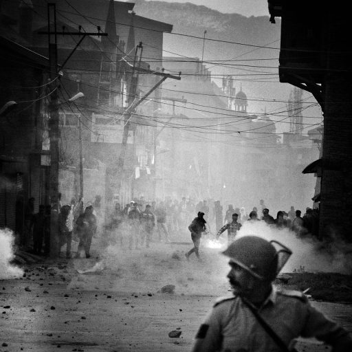 Amid dense tear gas smoke a security personnel walks past the protesters at Zaldagar area of Srinagar, Kashmir. On May 08, 2018. Government authorities imposed curfew in parts of the valley against the shutdown call given by (JRL) to protest the killings of 15 persons including armed rebels and unarmed civilians by the government forces at Kachdoora and Trukwangam in South Kashmir's District Shopian during past 56 hours.