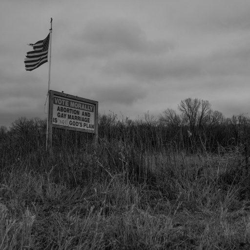 Photo by Brooklynn T. Kascel / VII Mentor Program. VOTE MORALLY, ABORTION AND GAY MARRIAGE IS NOT GOD'S PLAN", is written by hand on a sign next to a well-traveled road. Raymond, Iowa. 2021.