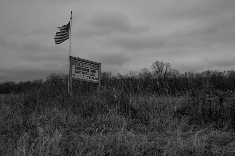 VOTE MORALLY, ABORTION AND GAY MARRIAGE IS NOT GOD'S PLAN", is written by hand on a sign next to a well-traveled road. Raymond, Iowa. 2021. © Brooklynn T. Kascel.