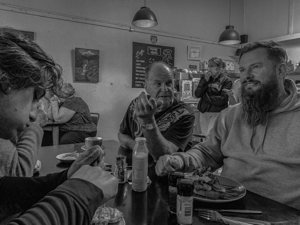 Three generations at breakfast. Twenty-year-old grandson Abraham Mataitini, 80 year old retired farmer Andy Davy, 51 year old son Aaron Davy. Arty Tarts cafe, Opunake, Taranaki, Aotearoa. Photo by Nick Netzler