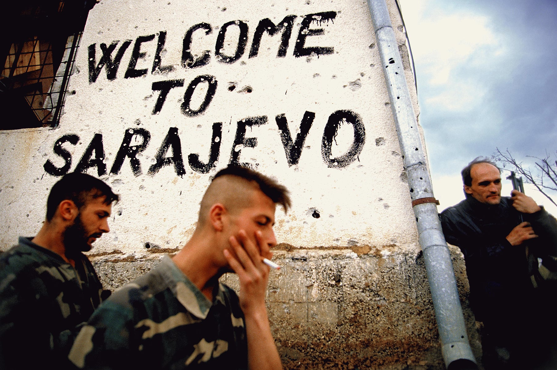 Bosnian soldiers smoke and take a break on the frontline next to a sign that says 'welcome to Sarajevo' in Sarajevo, Bosnia, in the fall of 1994. Trench warfare was fought all around the city of Sarajevo. © Ron Haviv / VII Photo
