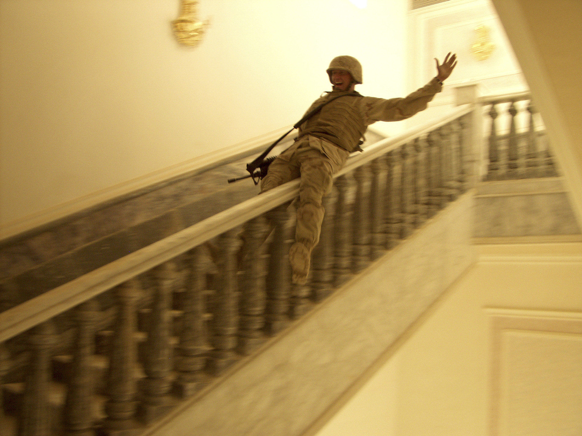 A U.S. Marine slides down the marble handrail in Saddam Hussein's extravagant palace built in his hometown of Tikrit. The enormous Palace contained rugs and antiquities worth hundreds of thousands of dollars before being looted by Iraqis and U.S. soldiers. Tikrit, Iraq, 2003. Photo by Ashley Gilbertson/VII