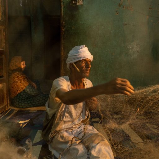 Darabala Abdel Hadi, 61, is seen fixing his fishing nets in his house in Fayoum, Egypt, on September 8, 2022. He is one of the victims of the deterioration of the lake, having worked as a fisherman for 20 years alongside his father in the area of Lake Qarun. The fish stocks in the lake have sharply declined due to severe pollution. Despite this, he has chosen to settle between Aswan and Fayoum, as he is unwilling to leave his land and roots. This displacement has resulted in the loss of ancestral roots and a deep emotional connection to the land. ©Fatma Fahmy for the VII Mentor Program.