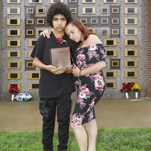 Troy, New York, 2019.
Billie Jean and her son Dasaun hold Billie Jean’s mother Rosanne’s crematory ashes in front of the wall where, after five years of saving from her disability checks, Billie Jean finally was able to purchase a mausoleum vault that would hold the sacred remains. In a community where there are few material comforts, the loss of family, even with fraught interactions, is devastating. Billie Jean has carried Rosanne’s ashes to every family event since her death, including Dasaun’s 18th Birthday and his high school graduation. © Brenda Ann Kenneally.