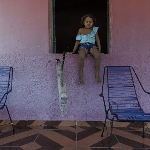 Luna Sofia, 5, sits at the windowsill of her grandmother’s home Maria Oneide Barros Carvalho, 67. In 2019, a state law established that Vila Esperança is a “Traditional Land of the Babaçu Coconut Breakers.” © Adriana Zehbrauskas.