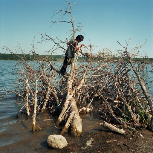 Young boy playing in the dried up bushes along the shore of Spirit Lake. August 2014. © Rena Effendi.