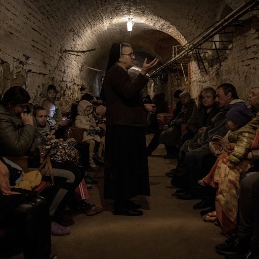 Sister Diogena Tereshkevych (C) tells stories to comfort people displaced from eastern Ukraine inside a bomb shelter during an air raid alert in the western Ukrainian city of Lviv, April 15, 2022. © Finbarr O’Reilly.