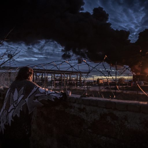 A woman watches a burning oil depot that local residents said had been by a Russian mortar barrage from across the Dnipro River in the southern Ukrainian city of Kherson, November 19, 2022. © Finbarr O’Reilly.