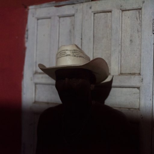 On March 4, 2020, Manoel Pankararu wears his cowboy hat in front of the window of his house located in the city of Resplendor, state of Minas Gerais, Brazil. He is one of the survivors of the Krenak Reformatory, the former indigenous prison. According to his testimony, he was brought by the military from his original land in the state of Pernambuco, northeast Brazil, where he was one of the local community leaders. The memories of that time are already fading away, and he no longer remembers how long he was imprisoned. What is known is that he was one of those who went through the whole 'integration' process not only in Resplendor but also in Carmésia. Currently, Manoel raises a few heads of cattle for a living in Resplendor. He is not allowed to return to Pernambuco because, after so much struggle, he is considered polluted by foreign culture and not recognized as a true member of his ethnic group, Pankararu. © Leonardo Carrato.