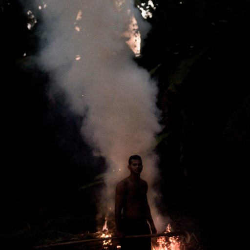 In April 2022, Sávio Pataxó burns dry leaves in the backyard of his house in the city of Carmésia, state of Minas Gerais, Brazil. Sávio is a member of the Pataxó youth group that gathers regularly to keep the traditions of their ethnicity alive by organizing traditional cultural events throughout the year. © Leonardo Carrato.