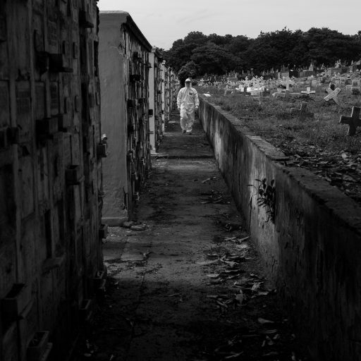 On April 15, 2020, during the Covid-19 pandemic, an undertaker walks down a corridor at the local cemetery before beginning one of the numerous burials scheduled for that day for those who had passed away due to Covid-19. The cemetery is considered the largest in town and is situated in a neighborhood called Caju, Rio de Janeiro, which is the preferred choice for most families residing in Rocinha due to its affordability. © Leonardo Carrato.