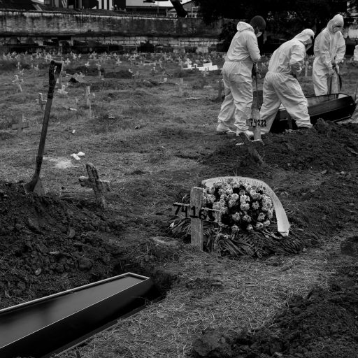 On April 15, 2020, during the Covid-19 pandemic, a wreath of flowers was placed by the family who couldn't be present while gravediggers lowered a coffin into a shallow grave at a local cemetery in Rio de Janeiro, Brazil. The cemetery is considered the largest one in town and is situated in a neighborhood called Caju, Rio de Janeiro, which is chosen by most families residing in Rocinha due to its affordability. © Leonardo Carrato/VII