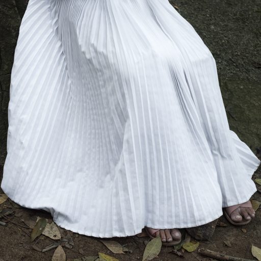 On June 15th, 2021, an evangelical apostle sat on a rock to commence a prayer on the sacred Mount Cardoso Fontes in the city of Rio de Janeiro, Brazil. The white skirt symbolizes a heightened spirituality as it adheres strictly to the norms of the Pentecostal religion. Mount Cardoso Fontes, situated in an ecological forest park in one of the primary neighborhoods of Rio de Janeiro, holds significant importance as a sacred place for evangelicals. The bond of faith with nature inspires evangelical believers to seek a closer relationship with God and purification of the soul. © Leonardo Carrato.