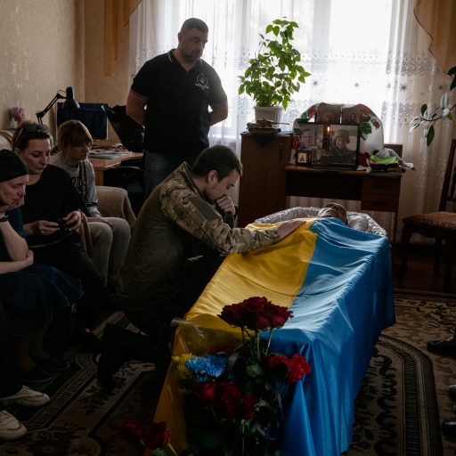 Friends and family mourned during the funeral of Ukrainian solider Dmytro Konobas, 43, while his unit member paid his respects, in Synyak, Ukraine, on Monday, May 15, 2023. Mr. Konobas was a widely-loved resident of Synyak, who helped villagers by bringing them food while at least 200 people sheltered in a school during the Russian occupation last year. He joined the military after the village was retaken by Ukraine, and was killed on May 7 in the Luhansk region. © Nicole Tung.