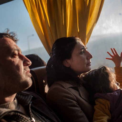 Tariq, left, Nisreen, and their five-year old daughter Roslyn, are seen on the day-long bus ride from Athens to the Greek-Macedonian border in the far north, as they continue their journey from Syria to Germany, on December 19, 2015. 

Over 1 million refugees and migrants have reached Europe's shores this year, overwhelming the continent and presenting the worst refugee crisis since World War II. Many thousands have been fleeing from conflict in Syria, Iraq, and Afghanistan, while thousands of others, from Bangladesh, Iran, and Pakistan seek better livelihoods. The recent  Euro 3bn deal struck between Turkey and the EU, intended to stanch the flow of people, has resulted in Turkish authorities cracking down on the smugglers and rounding up refugees, preventing them from making the sea crossing, but some continue to persist. © Nicole Tung.