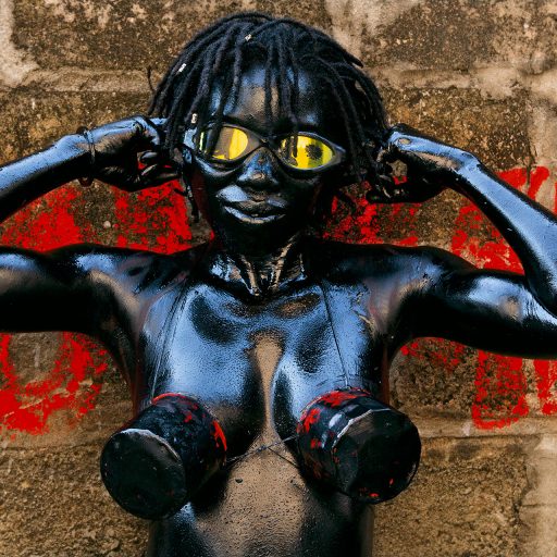 Democratic Republic of the Congo, 2012. The performing artist and photographer Julie Djikey (Kisalu Nkia Mbote collective) in the street in Kinshasa, protesting against cosmetics, pollution, and climate change. She has turned her body into a 'human car,' coating it with engine oil and ash from burnt tires, and wearing a bra made from oil filters. © Pascal Maitre.