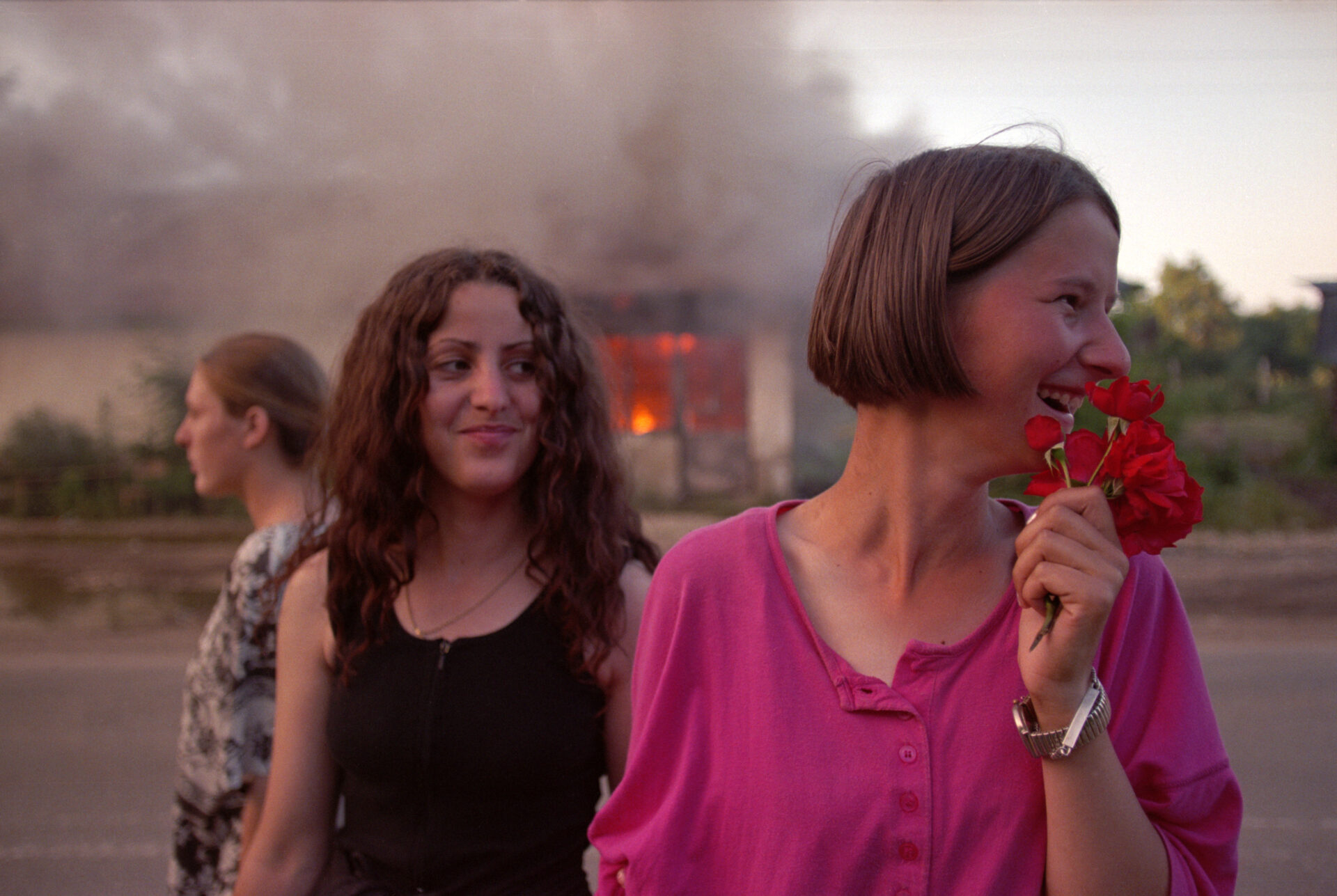 Ethnic Albanian Kosovar girls celebrate freedom in front of a burning house. NATO troops had just liberated Kosovo. The house in the background belonged to a Serb family. As an act of revenge, Albanians looted and burnt it. This is on the road from Mitrovica to Pristina. © Alexandra Boulat / The VII Foundation.