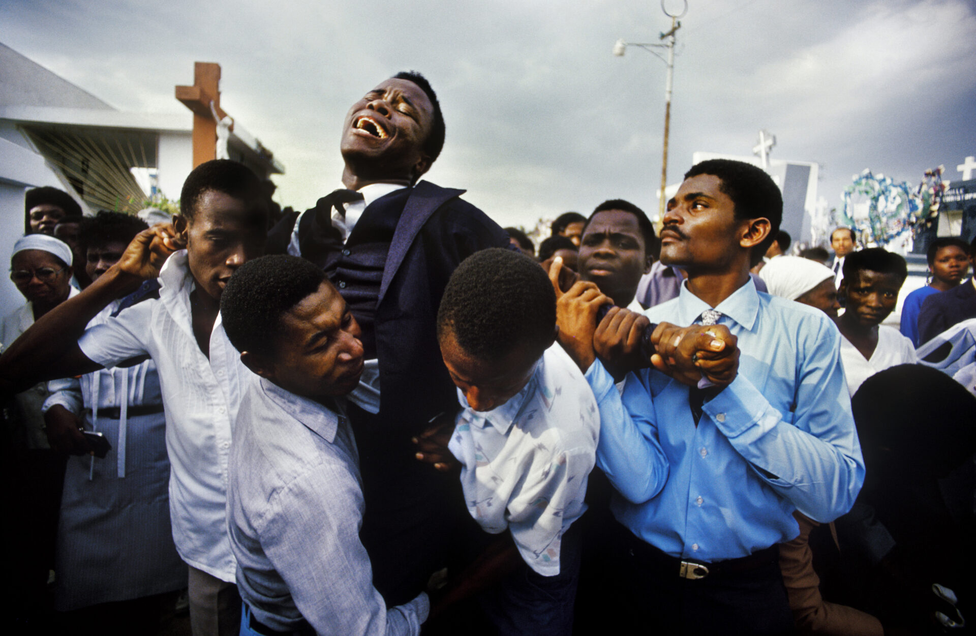 A young Haitian man writhes in grief at the funeral of his mother in the
National Cemetery in Pt-au-Prince, Haiti in November 1987, while his family and friends try to hold him back from the coffin. © Maggie Steber / VII.