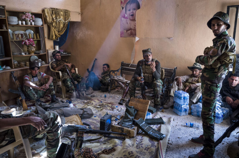 Members from the Asaib Ahl al-Haq militia pause for a moment to rest from fighting against ISIS insurgents in a house abandoned by its residents in the Al-Siniya district west of Baiji. Al-Siniya was a bastion of ISIS militants, and the urban warfare in its streets drained the Iraqi forces and slowed their advance to capture the area fully. The men rest and restock on ammunition less than 100 meters from the frontline with the insurgents. © Ali Arkady / VII.