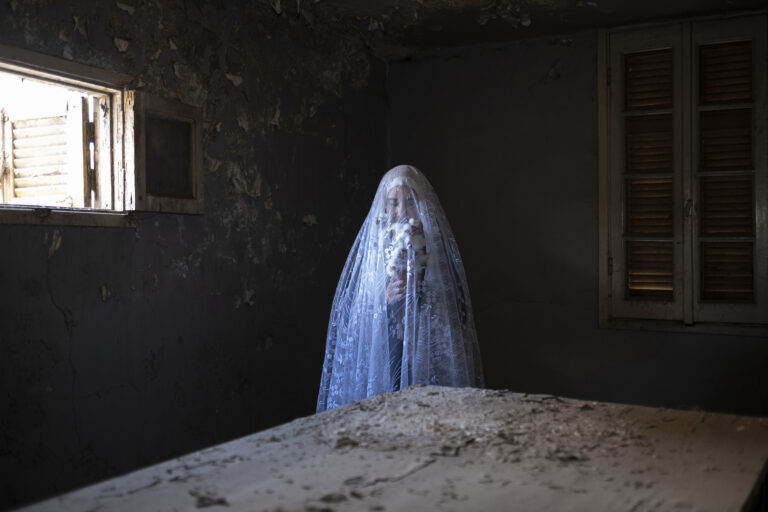 A self-portrait of the photographer holding a bouquet of cotton flowers, veiled, in her grandmother's old kitchen in the family’s home in El Mehalla El Kobra, Egypt, on Jan. 20, 2021. © Amina Kadous.