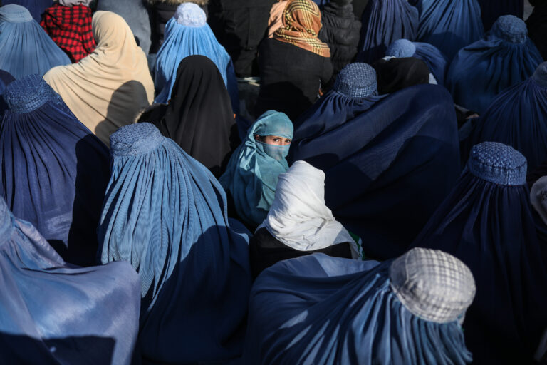 An Afghan girl sits in front of a bakery in the crowd with Afghan women waiting to receive bread in Kabul, Afghanistan, January 31, 2022. © Ali Khara.