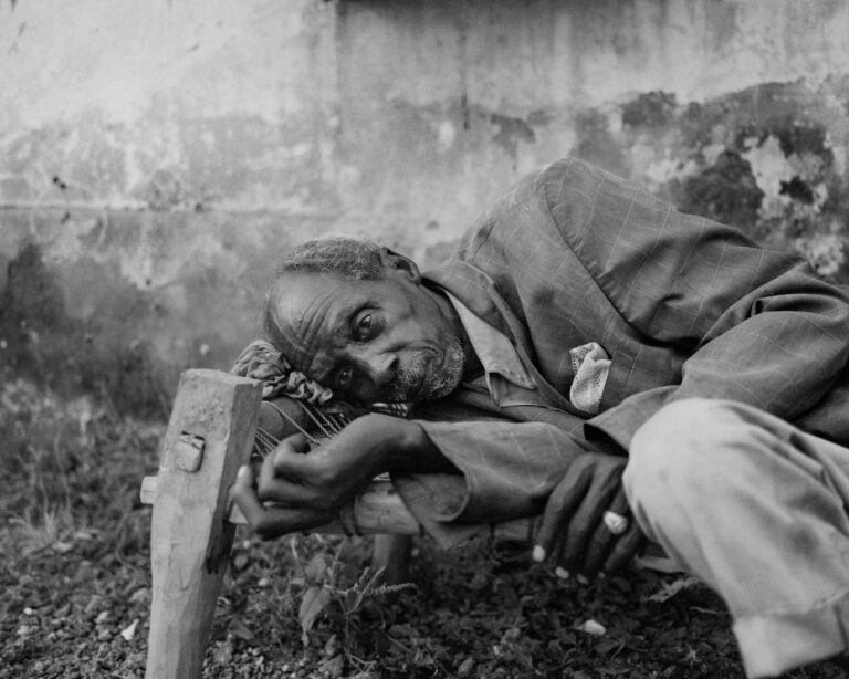 Mohammed Ibrahim, 60, lies on a wooden cot outside the MSF hospital in Abyei, resting in the shade after the long journey from Nyala. His daughter, Rehab, brought him south along with her three children after their town emptied under the pressure of the war. She says his mental health has worsened over the past months, and the family now waits together in Abyei, unsure of what comes next. Nicolò Filippo Rosso, 2025.