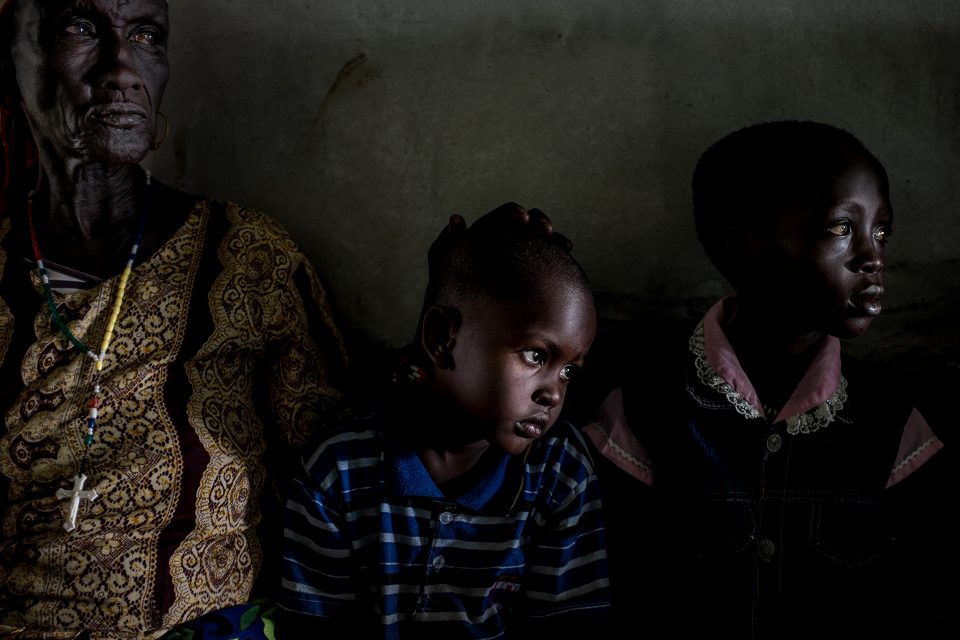 Photo by Ashley Gilbertson / VII. (L-R) Kenyan Anna Kiyonga (red and white head scarf, yellow patterned dress), 75, minds her grandson, Samuel Ekira (striped t-shirt), 4, and South Sudanese Eva James (denim shoulders jacket), 7, is looked after by her mother, Agnes Nadoi, 27, during a screening for patients potentially with Trachoma Trichiasis and other vision problems at the Sight Savers program held at Kakuma Mission Hospital, in Turkana West County, Kenya, on June 30, 2015. The two children in this photograph were the patients. Sight Savers is a British NGO that is diagnosing, curing, and preventing various eye conditions, including Trachoma, which has the highest incident rates Kenya in Turkana County. (Photo by Ashley Gilbertson / VII Photo)